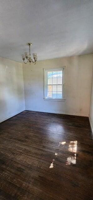 unfurnished room featuring an inviting chandelier, baseboards, and dark wood-type flooring