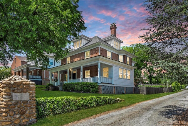view of property exterior with fence, brick siding, a chimney, covered porch, and a yard