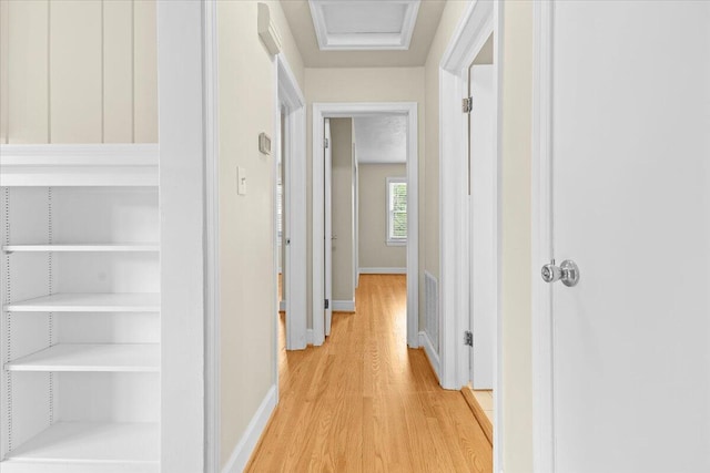 hallway with light wood-type flooring, attic access, and baseboards