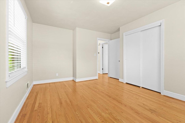 unfurnished bedroom with baseboards, a closet, light wood-type flooring, and visible vents