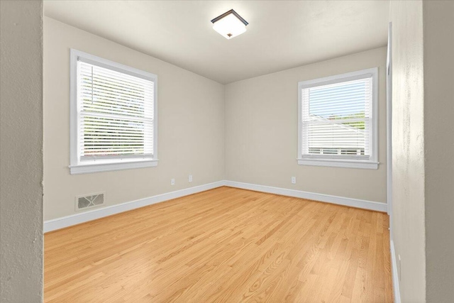 empty room with baseboards, visible vents, and light wood finished floors
