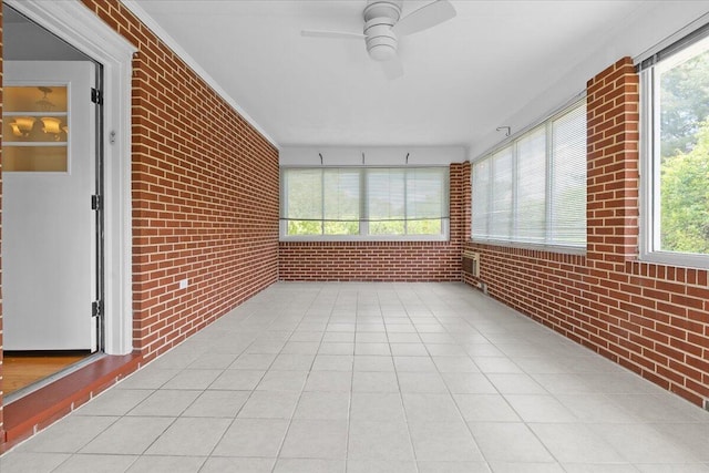 unfurnished sunroom with brick wall, ceiling fan, and tile patterned floors