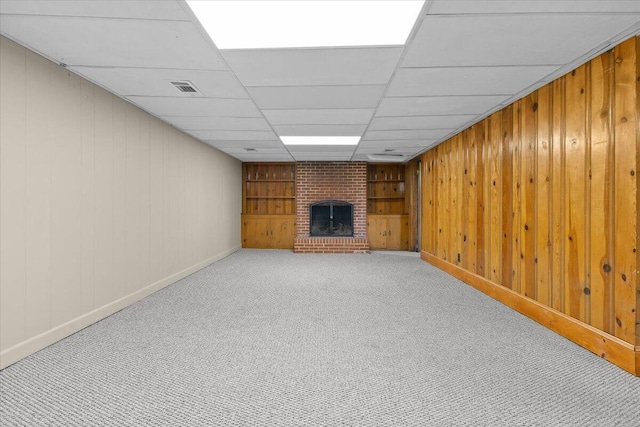 finished basement featuring visible vents, a brick fireplace, baseboards, wooden walls, and light colored carpet