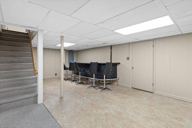 finished basement featuring a bar, a paneled ceiling, and stairway