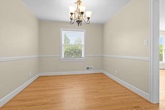 spare room featuring a healthy amount of sunlight, a notable chandelier, wood finished floors, and visible vents