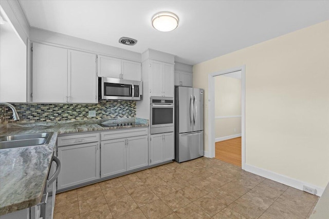 kitchen featuring baseboards, appliances with stainless steel finishes, a sink, and tasteful backsplash