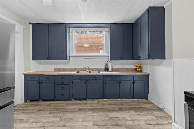 kitchen with light wood-style floors, a sink, blue cabinets, and light countertops