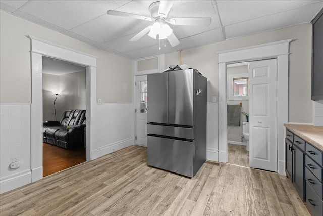 kitchen featuring freestanding refrigerator, ceiling fan, light wood finished floors, and a wainscoted wall