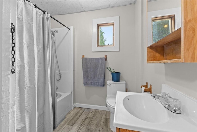 bathroom with toilet, shower / bathtub combination with curtain, a paneled ceiling, baseboards, and wood finished floors