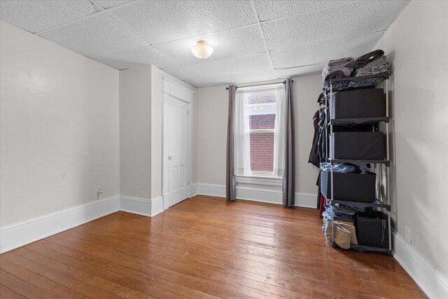 interior space with baseboards, a drop ceiling, and hardwood / wood-style flooring