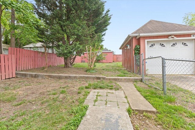 view of yard featuring fence, an outdoor structure, an attached garage, and driveway
