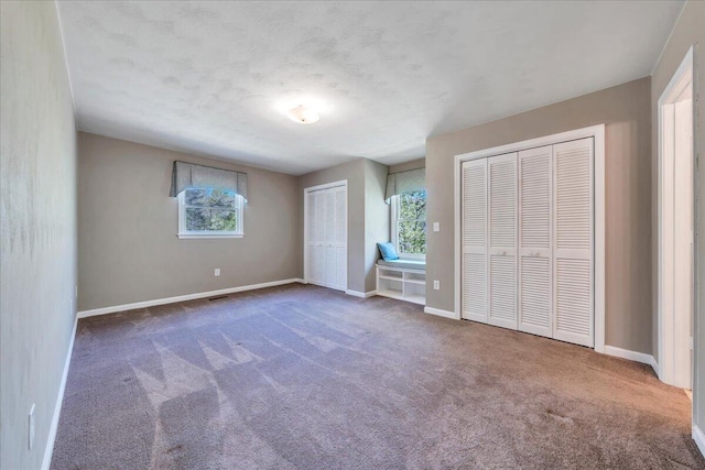 unfurnished bedroom featuring carpet floors, baseboards, and two closets
