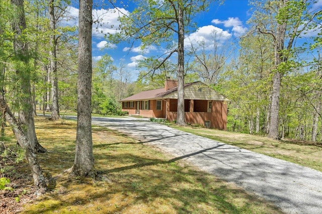 view of front of house featuring driveway, a chimney, and a front lawn