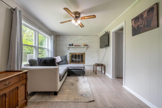 living room featuring ceiling fan, light wood-style flooring, a brick fireplace, crown molding, and baseboards