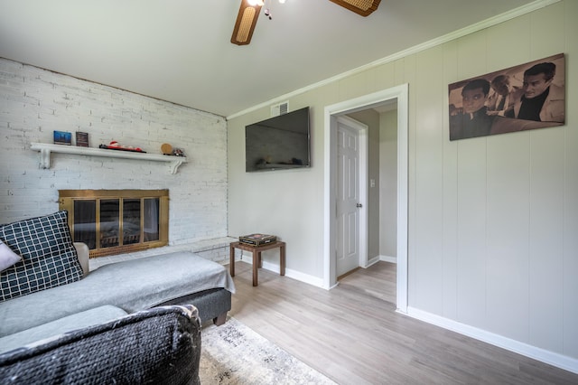 living area featuring wood finished floors, baseboards, a brick fireplace, ornamental molding, and ceiling fan