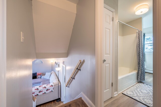 staircase featuring wood finished floors, a baseboard heating unit, and baseboards