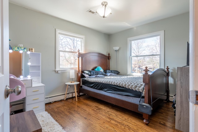 bedroom featuring a baseboard heating unit, wood finished floors, and multiple windows