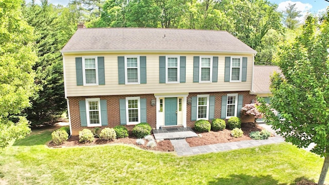 colonial-style house with brick siding, a front yard, and a chimney