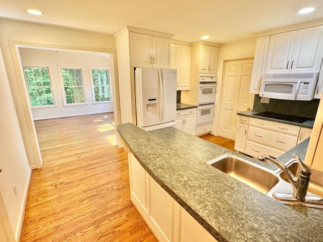 kitchen featuring dark countertops, a sink, light wood finished floors, white appliances, and white cabinetry