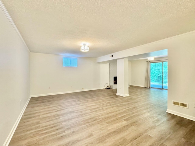 basement with a textured ceiling, visible vents, ornamental molding, and wood finished floors