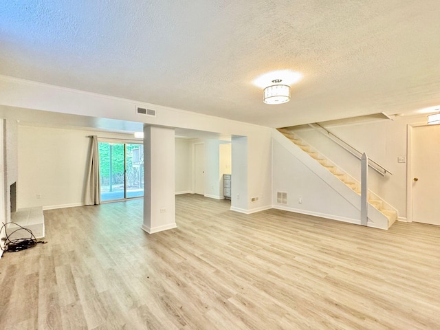 unfurnished living room featuring stairway, light wood-style floors, a textured ceiling, and visible vents