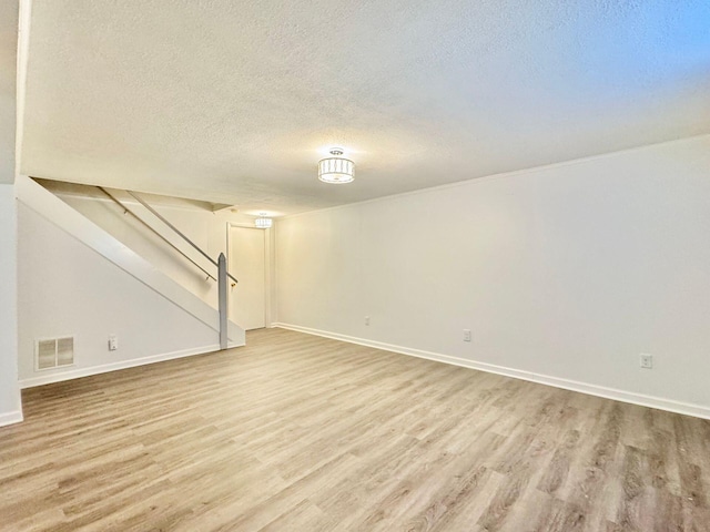 finished below grade area with a textured ceiling, visible vents, wood finished floors, baseboards, and stairs