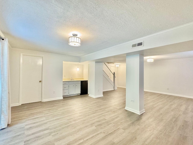 unfurnished living room with a textured ceiling, baseboards, light wood-type flooring, visible vents, and stairway