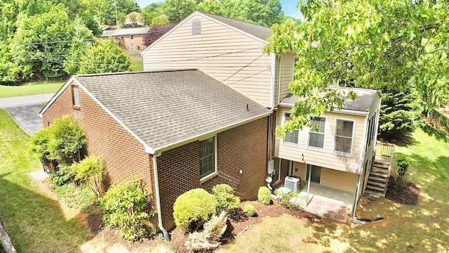 view of property exterior with cooling unit, roof with shingles, brick siding, a yard, and stairway