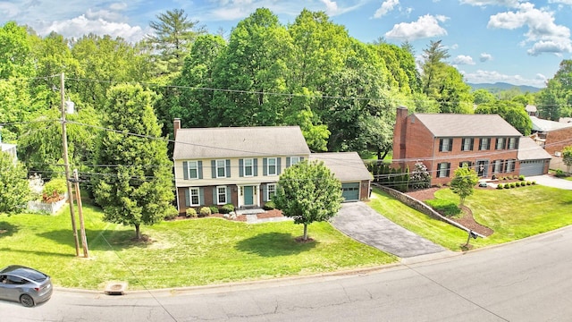 colonial inspired home with an attached garage, aphalt driveway, a chimney, and a front yard