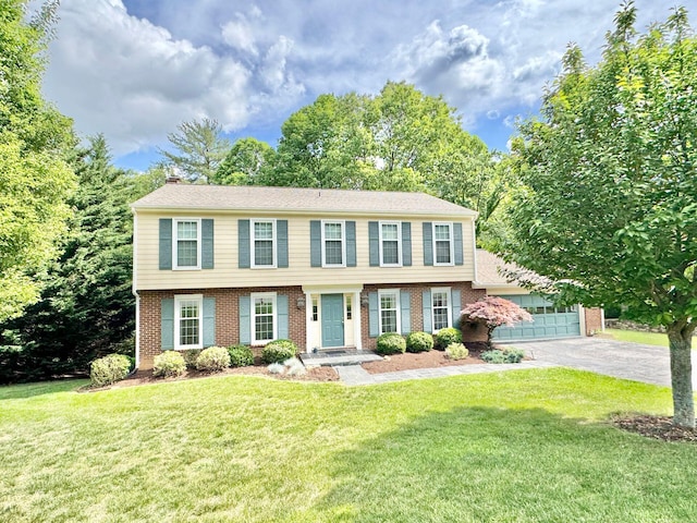 colonial-style house featuring a chimney, a garage, brick siding, aphalt driveway, and a front lawn