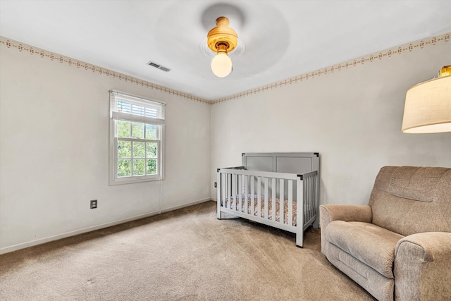 carpeted bedroom featuring visible vents, a ceiling fan, baseboards, and a crib