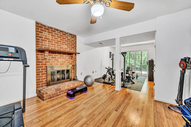 exercise area with baseboards, a ceiling fan, a brick fireplace, and wood finished floors