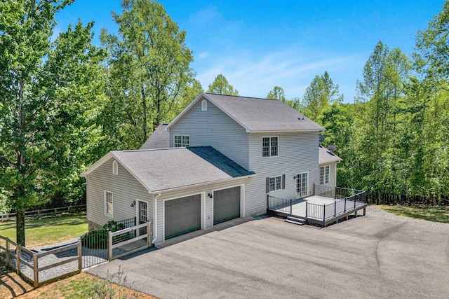 view of front of property featuring fence, a deck, roof with shingles, an attached garage, and driveway