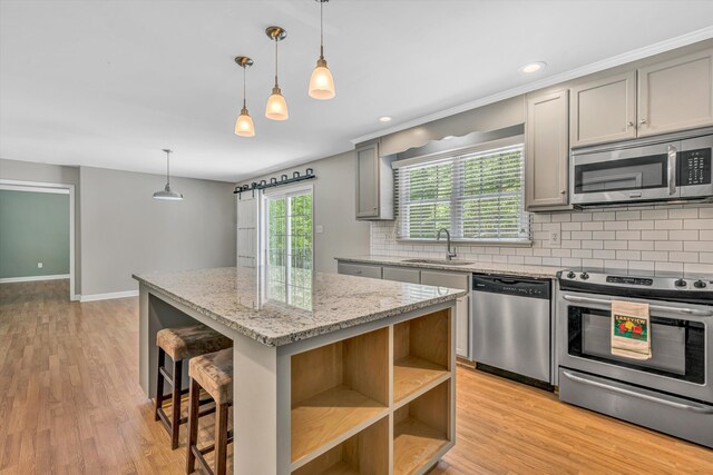 kitchen featuring gray cabinets, backsplash, appliances with stainless steel finishes, a center island, and a sink