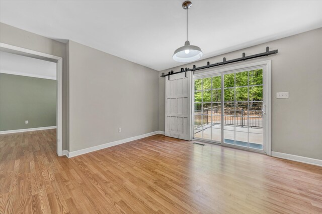unfurnished dining area with baseboards, a barn door, and light wood-style flooring