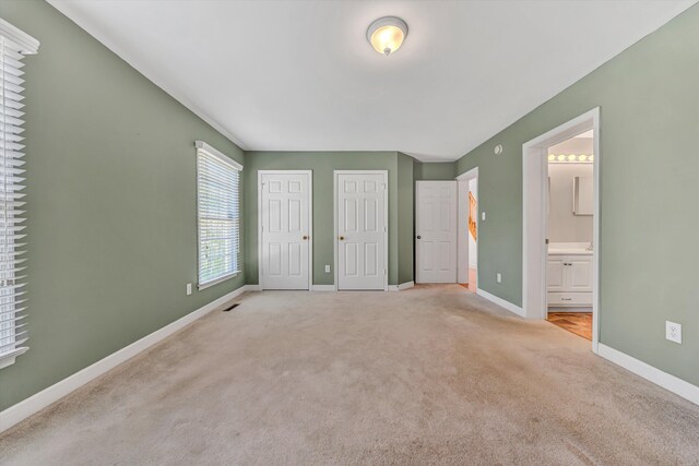 unfurnished bedroom featuring baseboards, ensuite bathroom, two closets, and carpet flooring