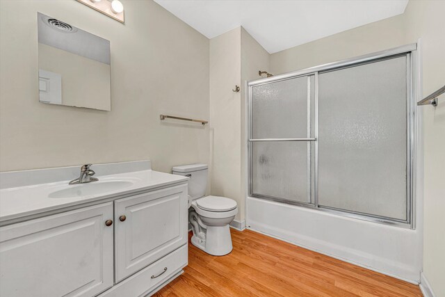 bathroom with vanity, toilet, wood finished floors, visible vents, and bath / shower combo with glass door