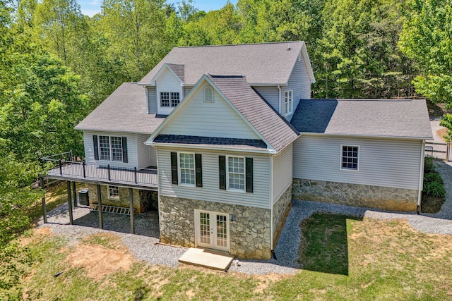 rear view of house with stone siding, a deck, roof with shingles, french doors, and a lawn