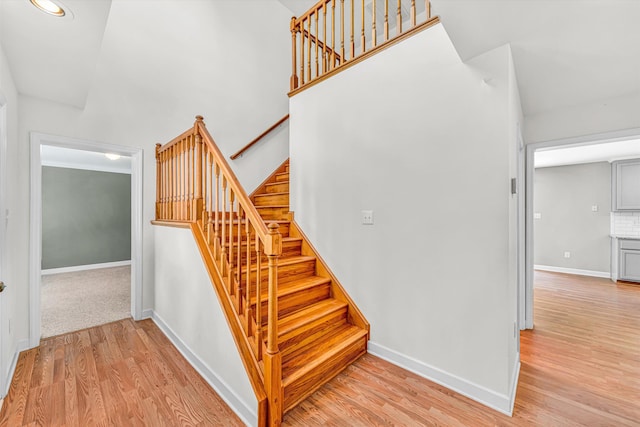 stairway with baseboards, recessed lighting, wood finished floors, and a towering ceiling