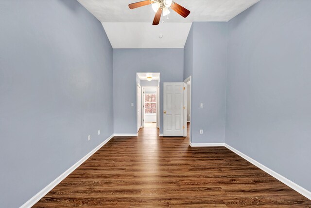 unfurnished room featuring baseboards, ceiling fan, vaulted ceiling, and dark wood-style floors