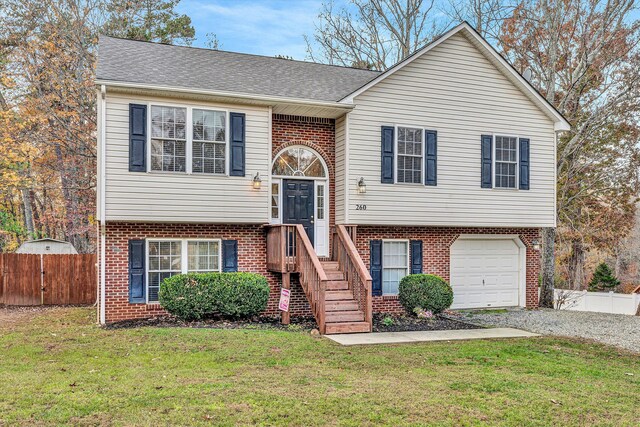 raised ranch with brick siding, an attached garage, fence, and a front yard