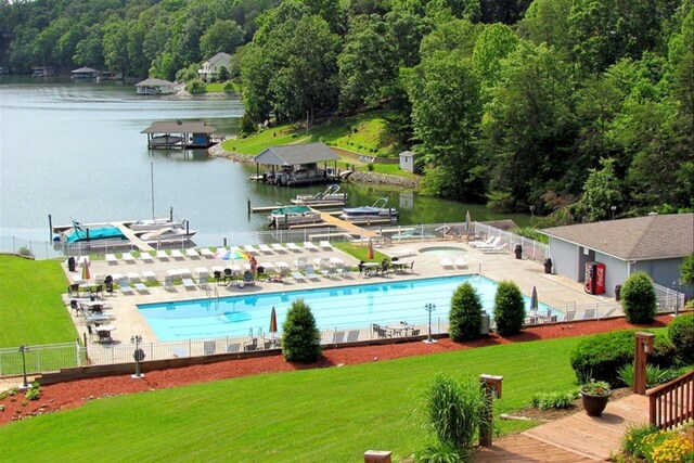 pool featuring a patio area, fence, a wooded view, a yard, and a water view