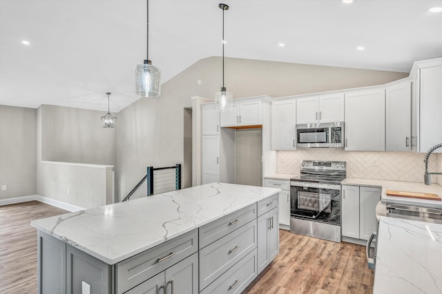kitchen with backsplash, vaulted ceiling, gray cabinetry, light wood finished floors, and stainless steel appliances