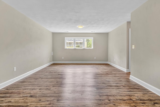 empty room with dark wood-type flooring, a textured ceiling, and baseboards