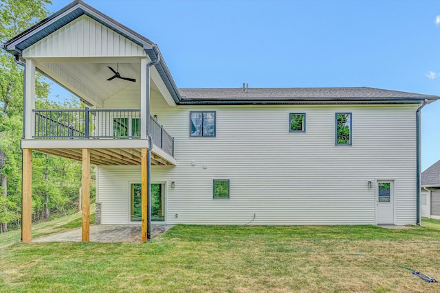 rear view of house with a shingled roof, a wooden deck, a patio area, a ceiling fan, and a yard