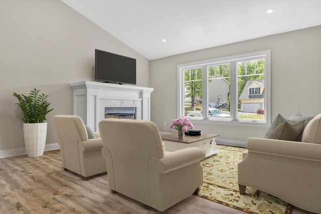 living area with light wood-type flooring, baseboards, vaulted ceiling, and a premium fireplace