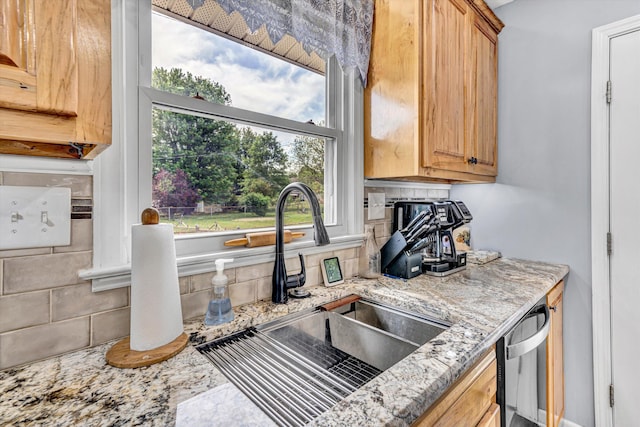 kitchen with backsplash, stainless steel dishwasher, light stone counters, and a sink