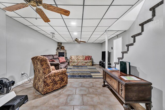tiled living area featuring baseboards, a ceiling fan, stairs, and a drop ceiling