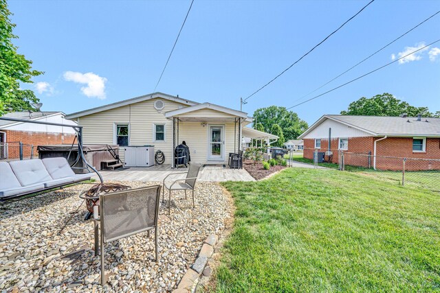 back of property featuring a patio area, a hot tub, a fenced backyard, a yard, and a fire pit