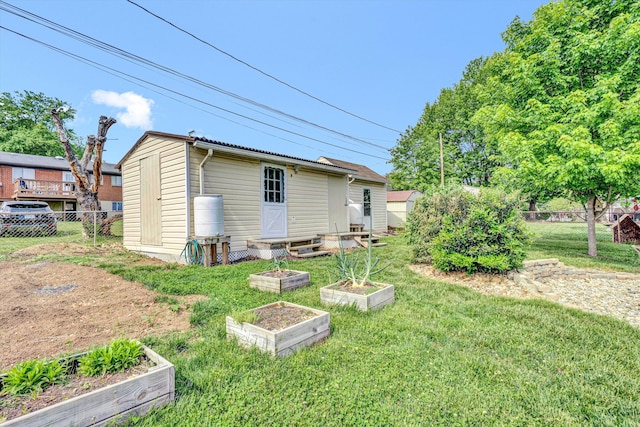rear view of house featuring fence, an outdoor structure, a yard, and a garden